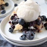 Scoop of vanilla ice cream on top of blueberry cobbler on a white plate.