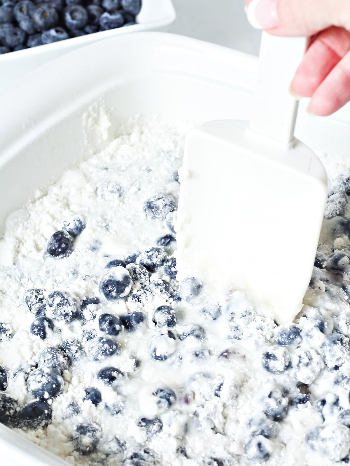 Stirring water into cake mix and blueberries in a white dish.