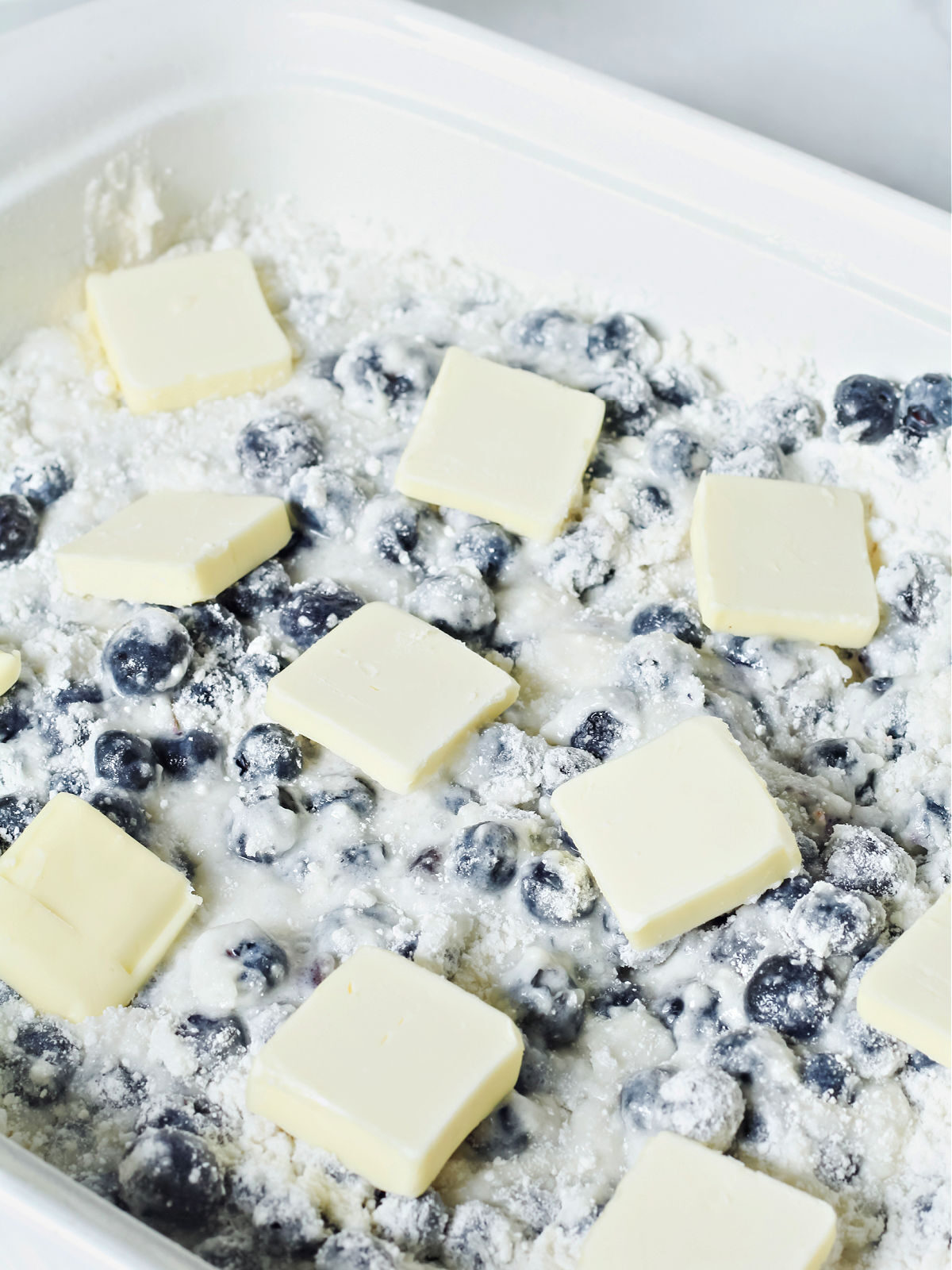 White cake mix, blueberries, and pats of butter in a baking dish.