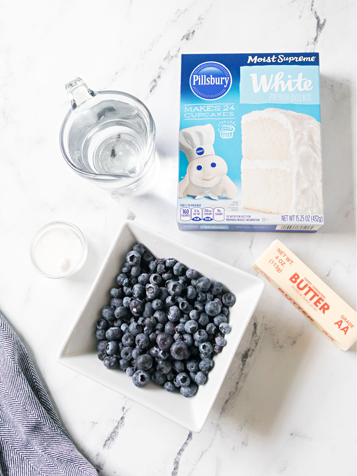 Box of white cake mix, blueberries, stick of butter, and water.