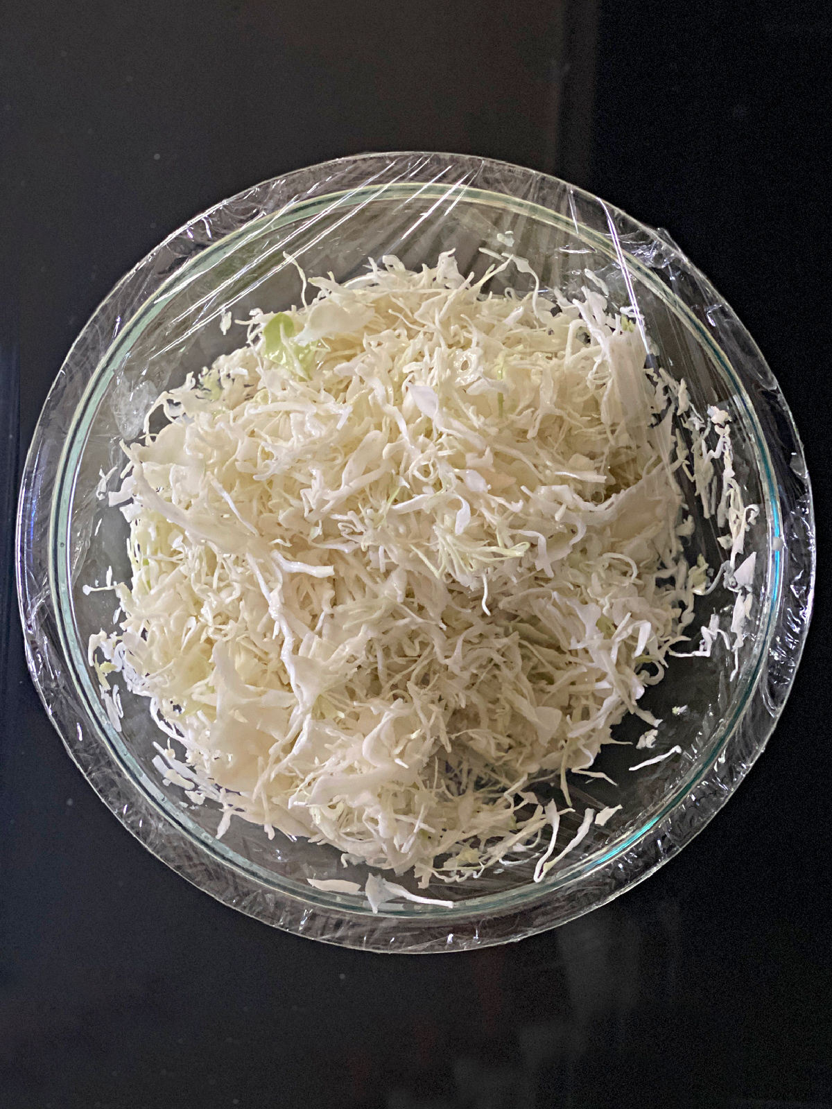 Vinegar Slaw Bowl of shredded cabbage with vinegar covered with plastic wrap.