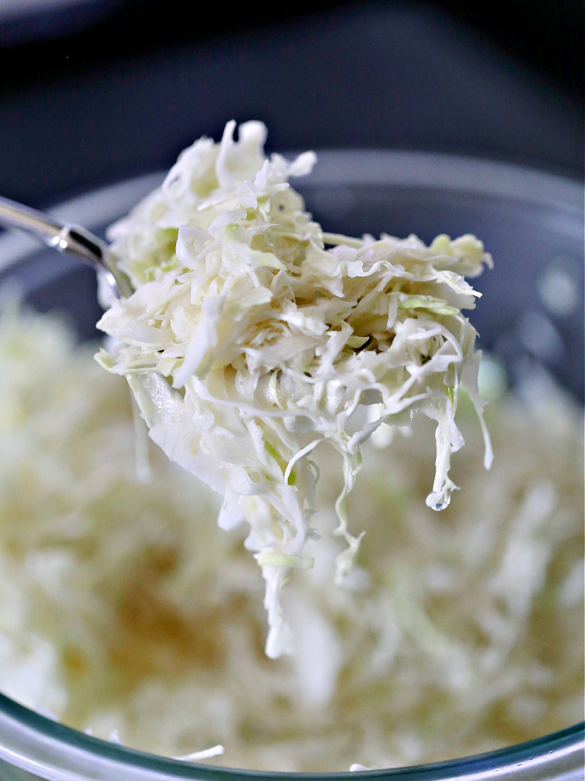 Spoon with vinegar slaw being held over a glass bowl.