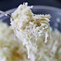 Spoon with vinegar slaw being held over a glass bowl.