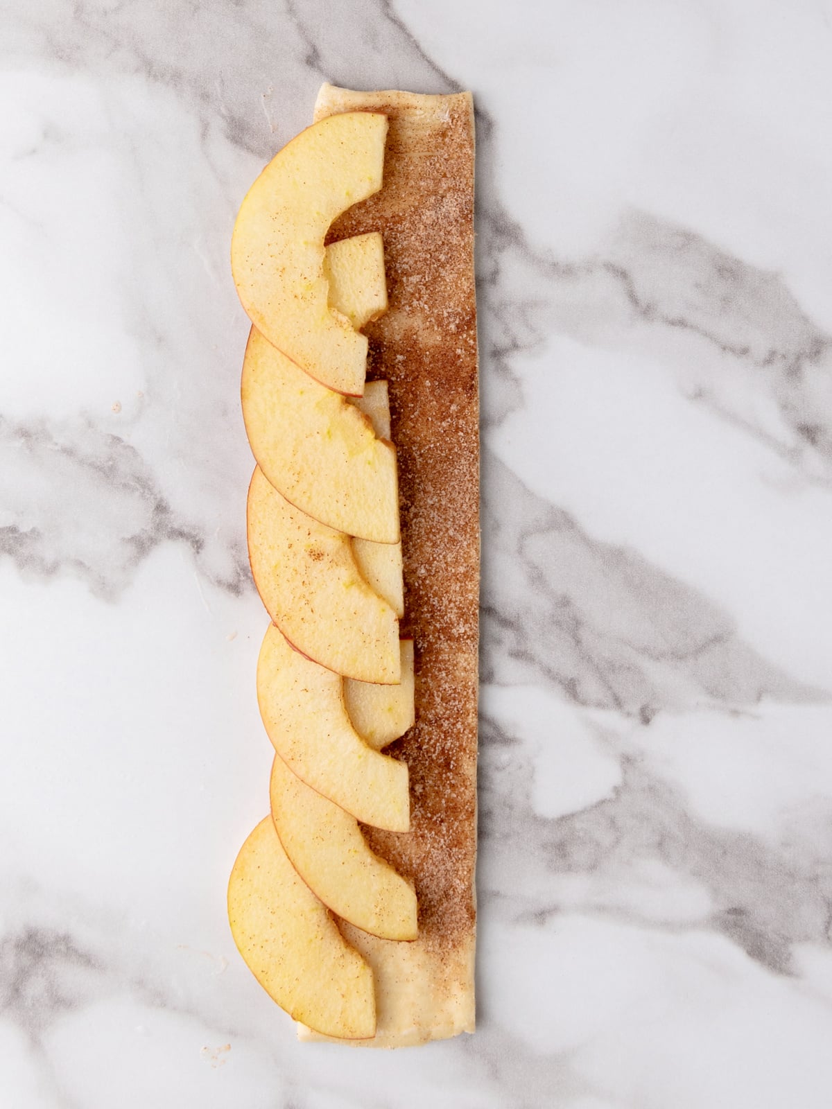 Apple slices on top of a strip of puff pastry covered with cinnamon sugar.