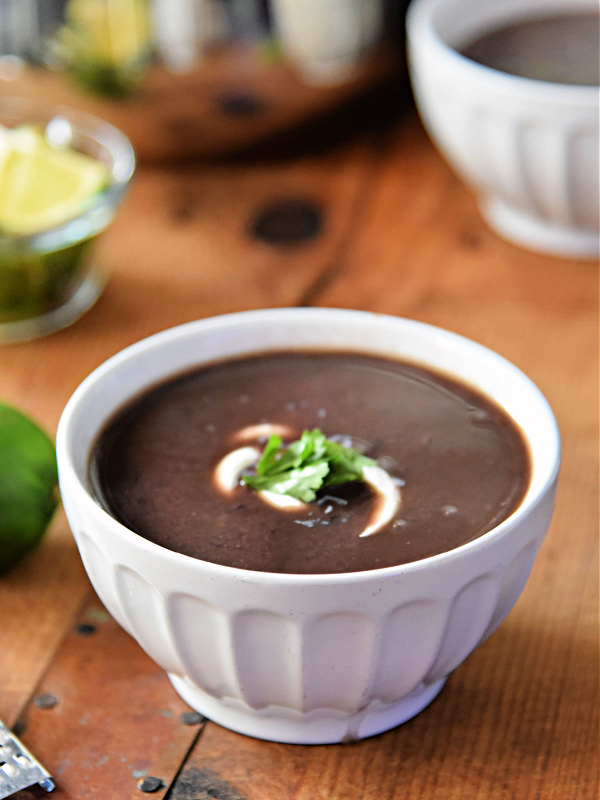 White bowl filled with black bean soup topped with sour cream and cilantro.