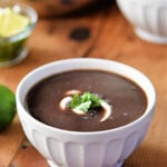 White bowl filled with black bean soup topped with sour cream and cilantro.
