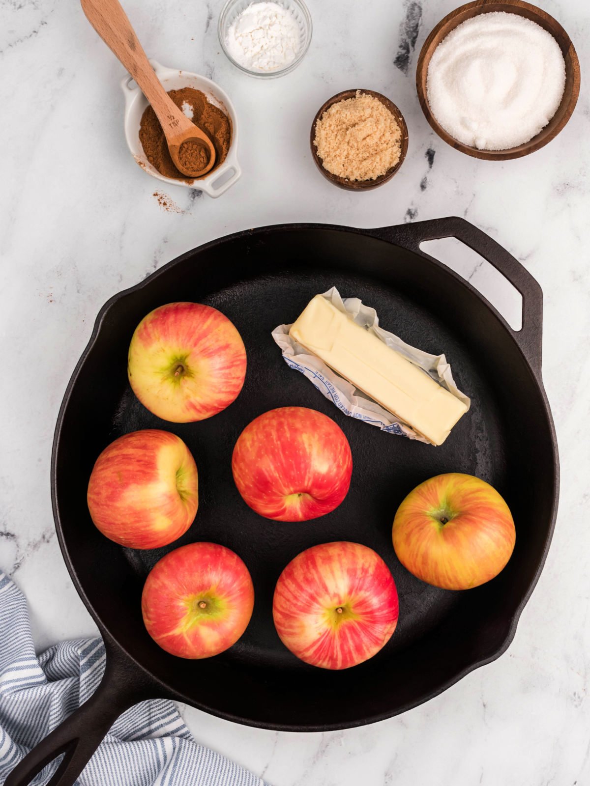 Cast iron skillet with six apples and a stick of butter.