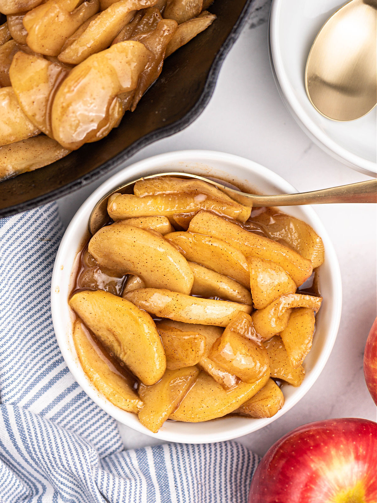 Cast iron skillet next to a white bowl with fried apples.
