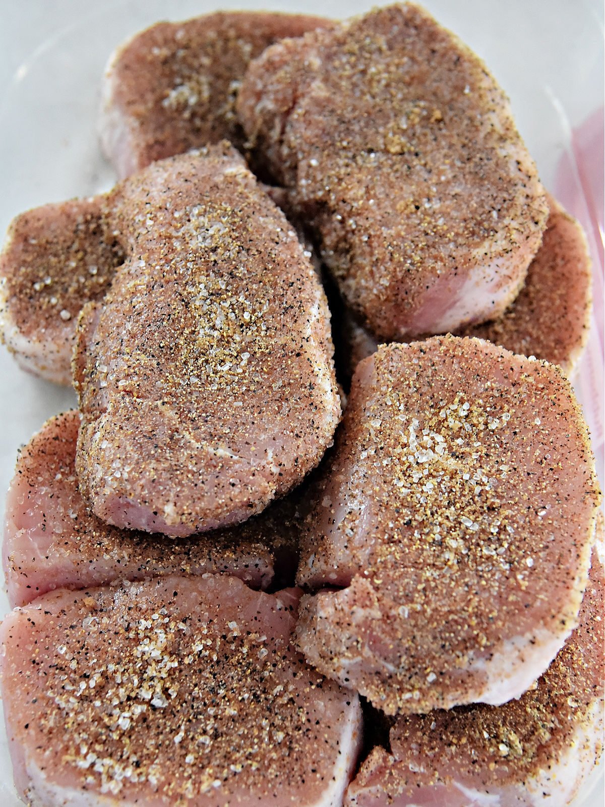 Raw pork chops covered in seasoning blend in a plastic container.