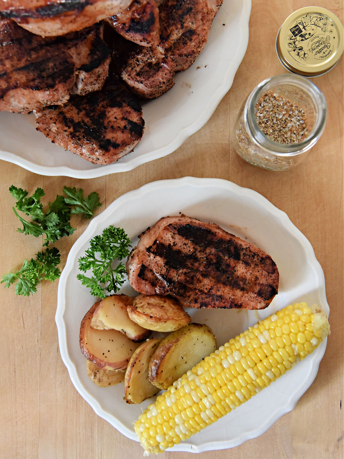Grilled pork chop, potatoes, and corn on a white plate.