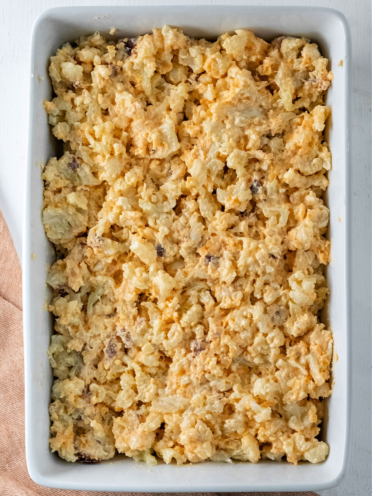 Unbaked cauliflower casserole in a white 9x13 baking dish.