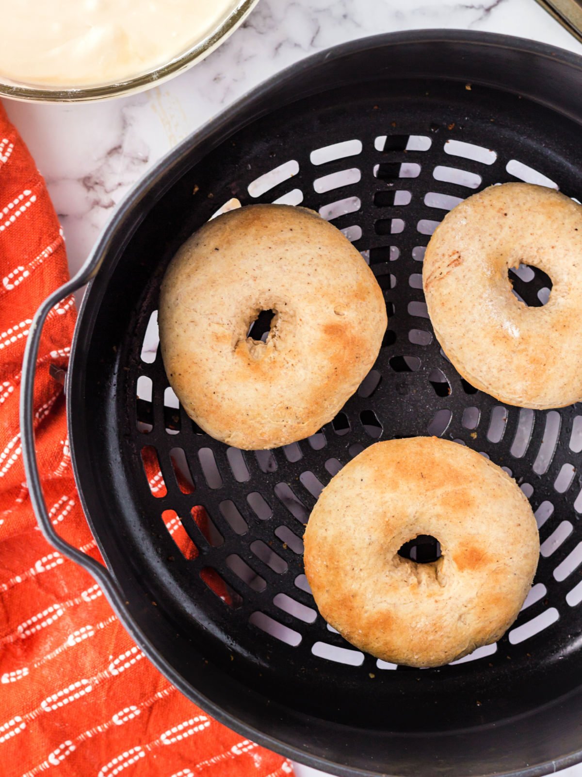 Three doughnuts in an air fryer basket.