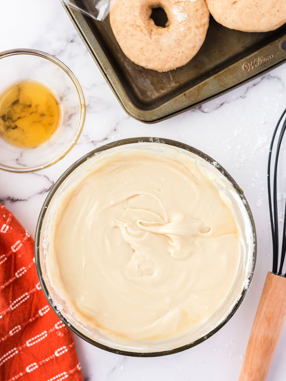 Glass bowl filled with maple glaze by pan of doughnuts.