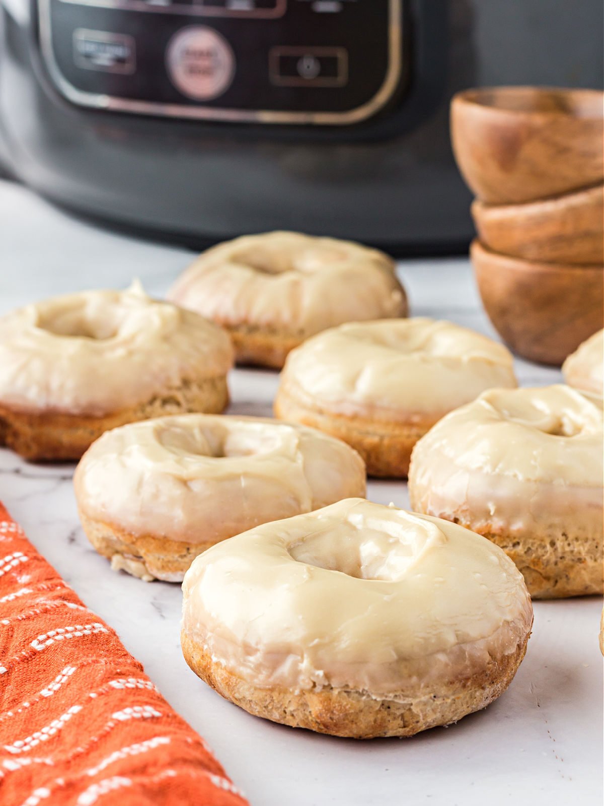 Glazed maple doughnuts in front of an air fryer.