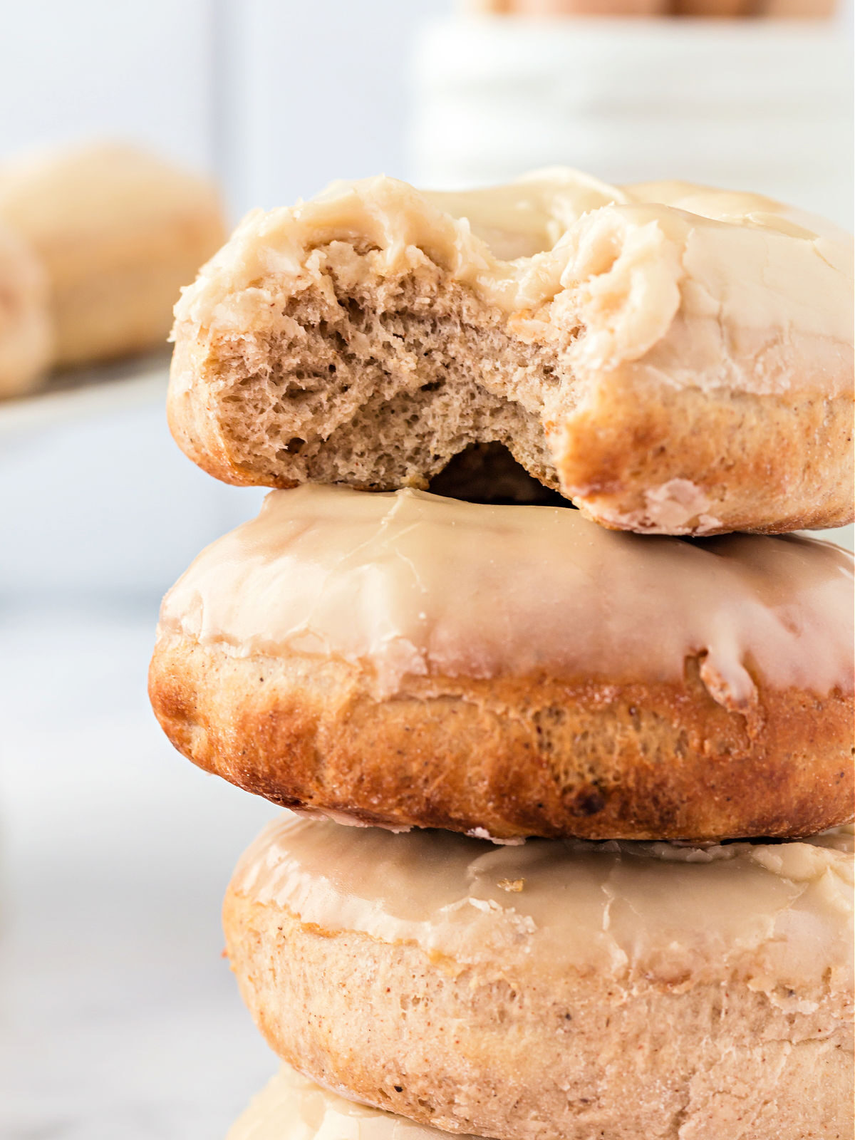 Stack of glazed maple doughnuts with top doughnut missing a bite.