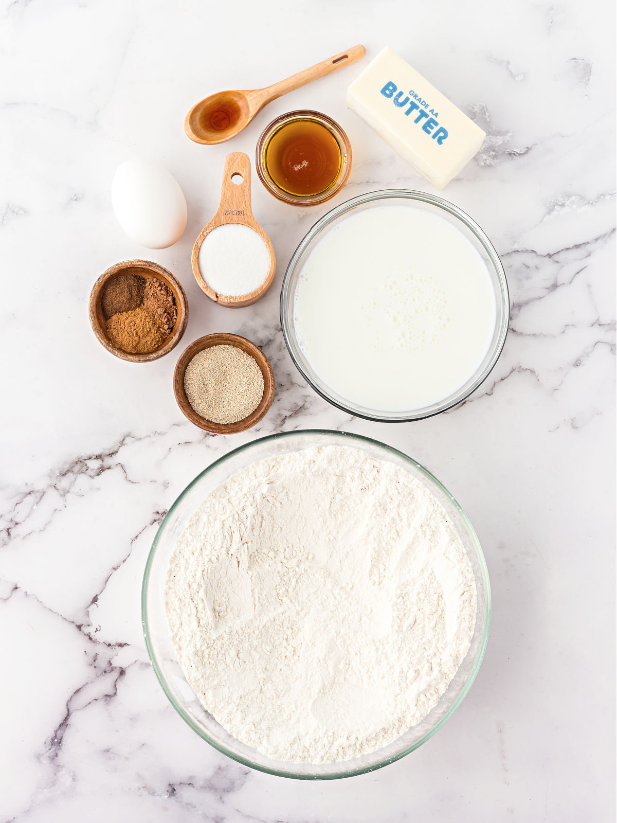 Flour, milk, yeast, spices, maple syrup, and butter on a marble counter.