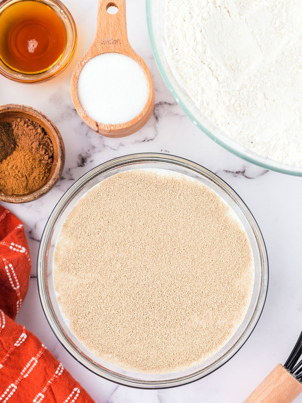 Bowl of milk, yeast, and sugar by a bowl of flour.