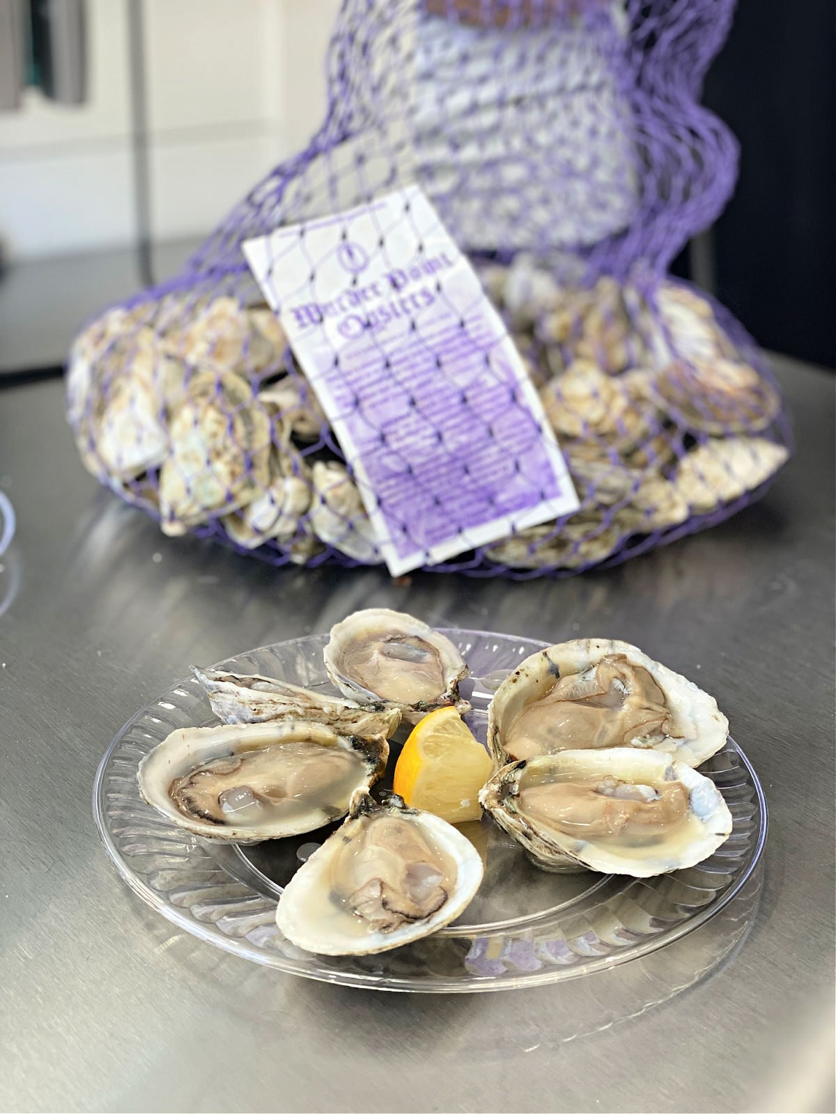 Plate with six oyster shells cracked open with a lemon wedge.