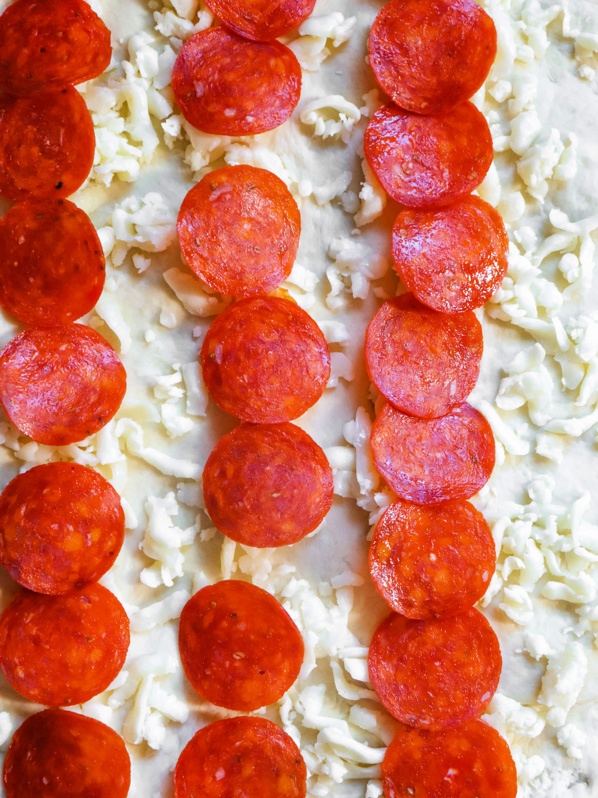 Three rows of pepperoni on top of mozzarella cheese and pizza dough.