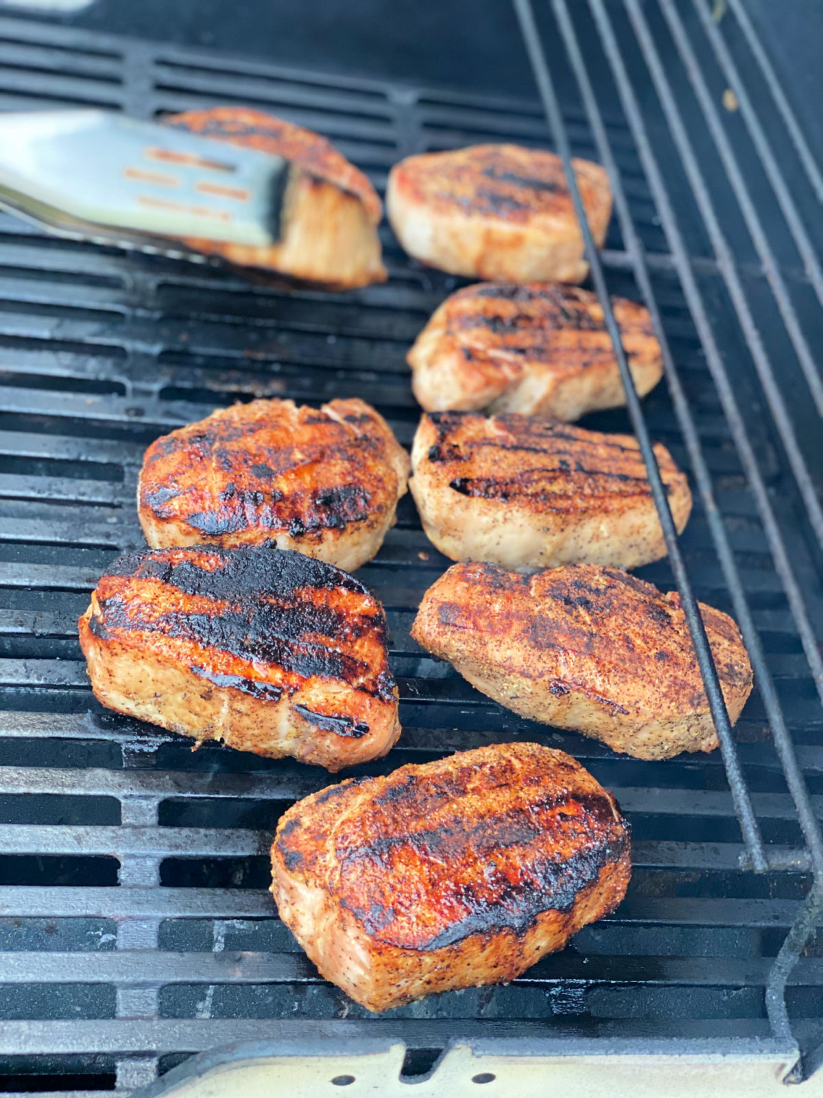 Nine pork chops cooking on a gas grill.
