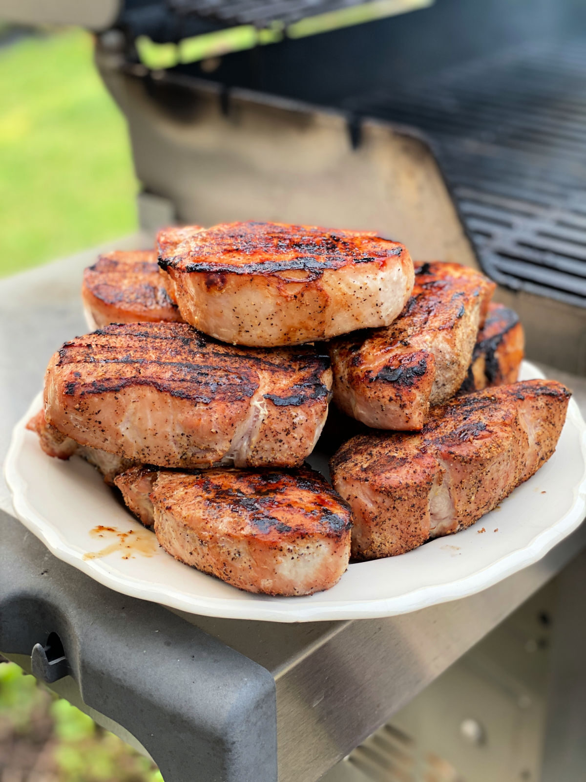 Platter of grilled pork chops next to a gas grill.