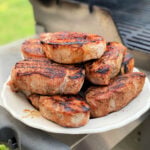 Platter of grilled pork chops next to a gas grill.