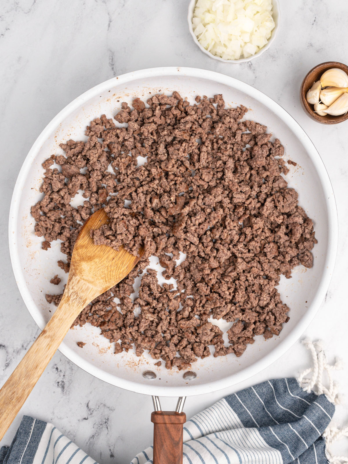 Cooked ground beef in a white skillet with a wooden spoon.