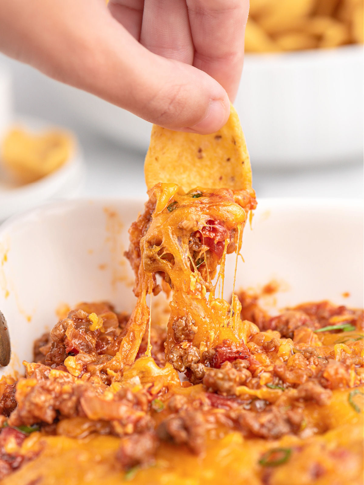 Make this Sloppy Joe Dip for your next tailgate! Woman's hand holding a corn chip with scoop of sloppy Joe dip.