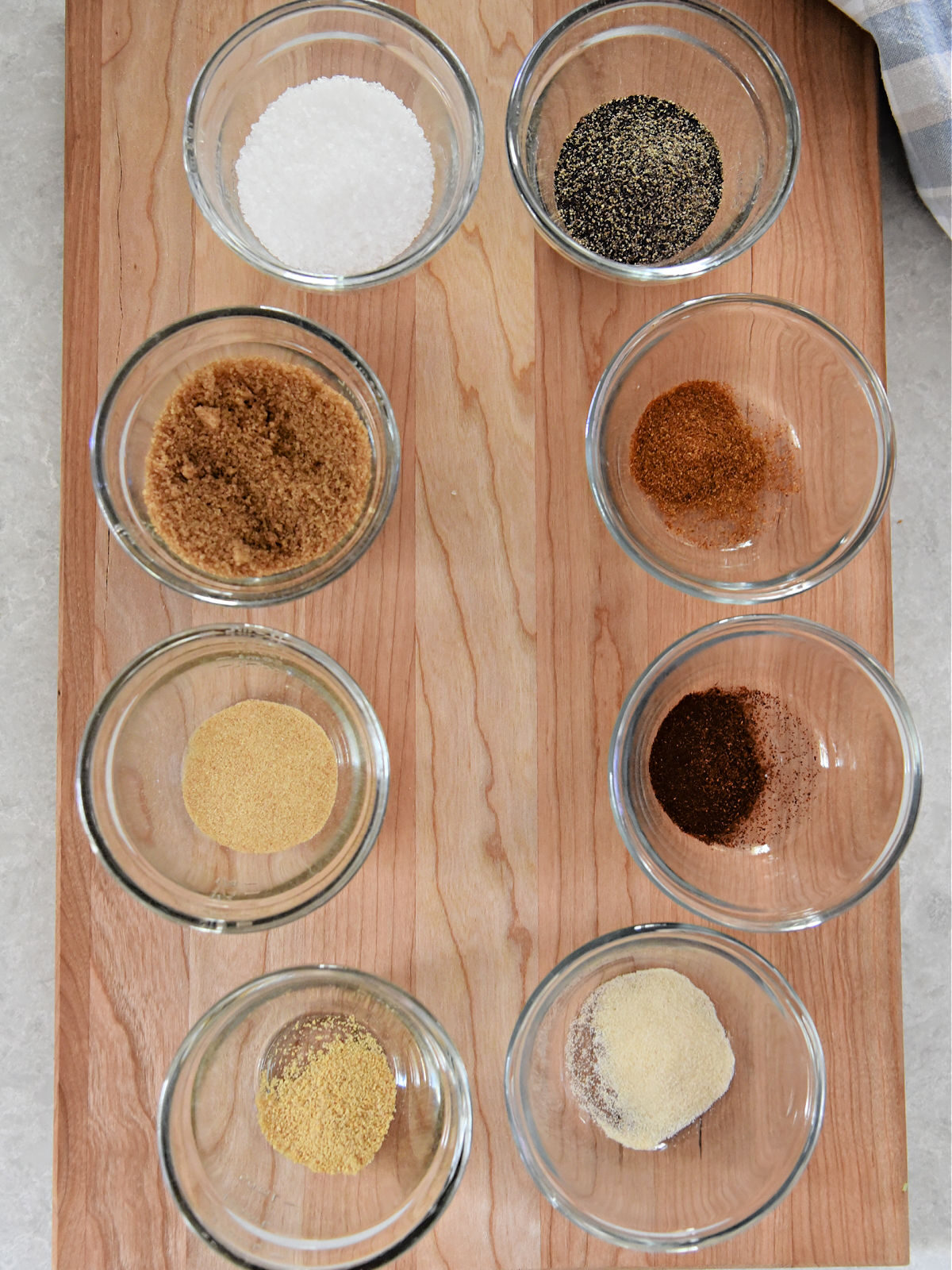 Spices in small glass bowls on top of a wooden cutting board.