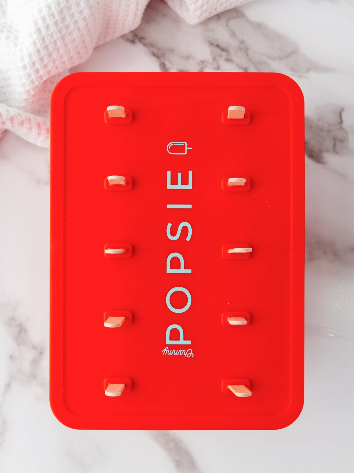 Red popsicle mold with popsicle sticks sticking out.