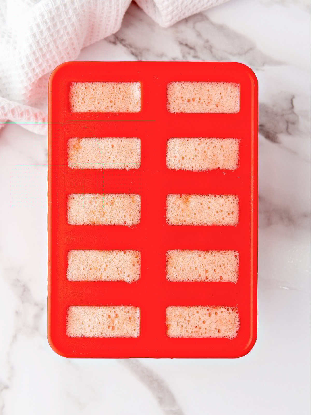 Strawberry popsicle filling in a popsicle mold.