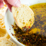 Slice of French bread being dipped into a bowl of olive oil dip.