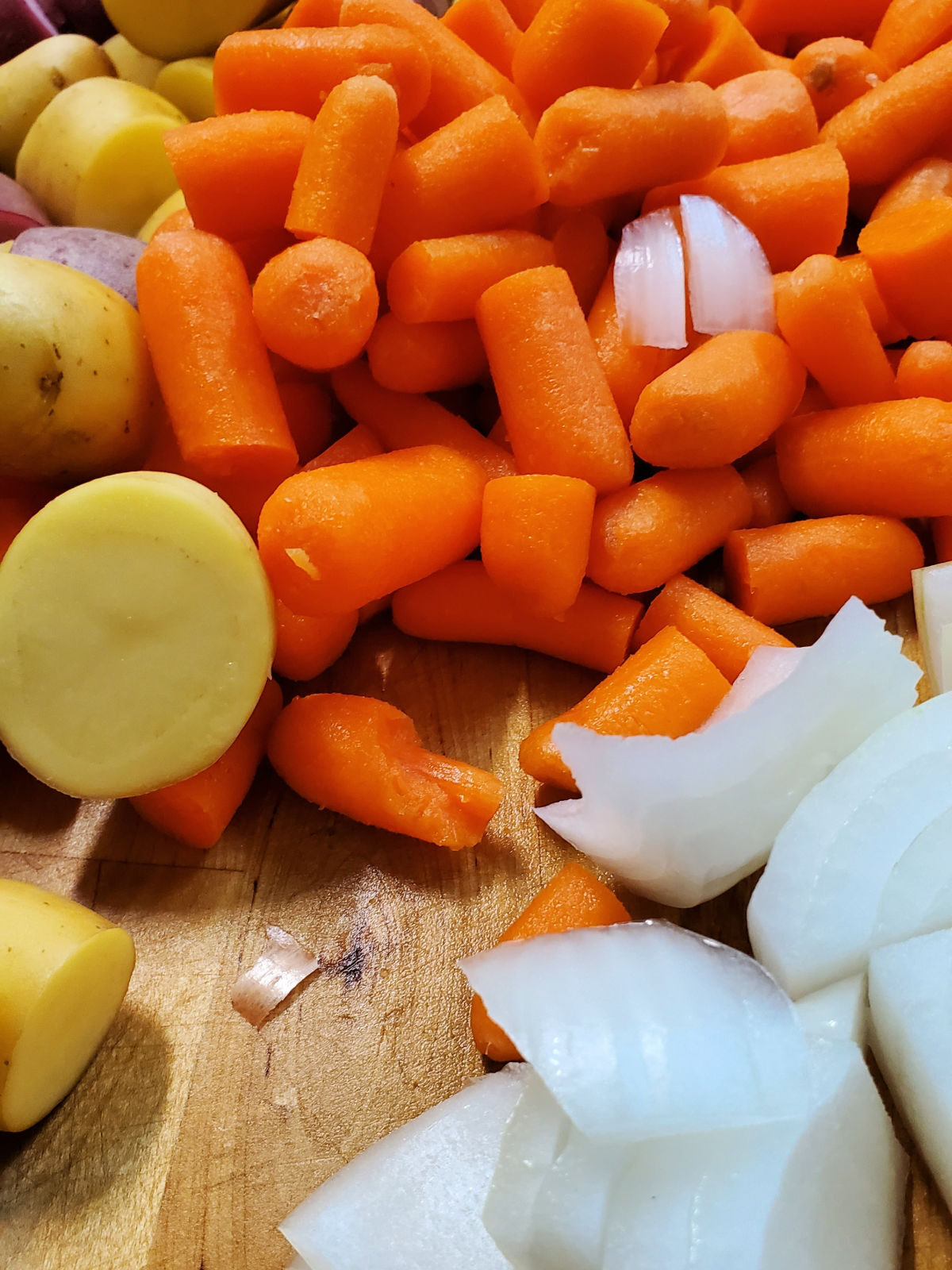 Cutting board with potatoes, carrots, and onions.
