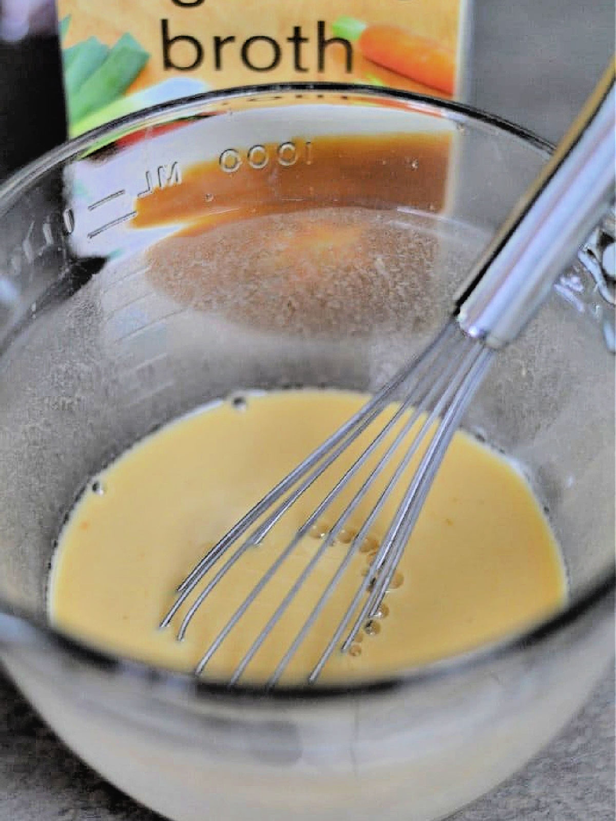 Vegetable broth and cornstarch in a glass bowl with a whisk.