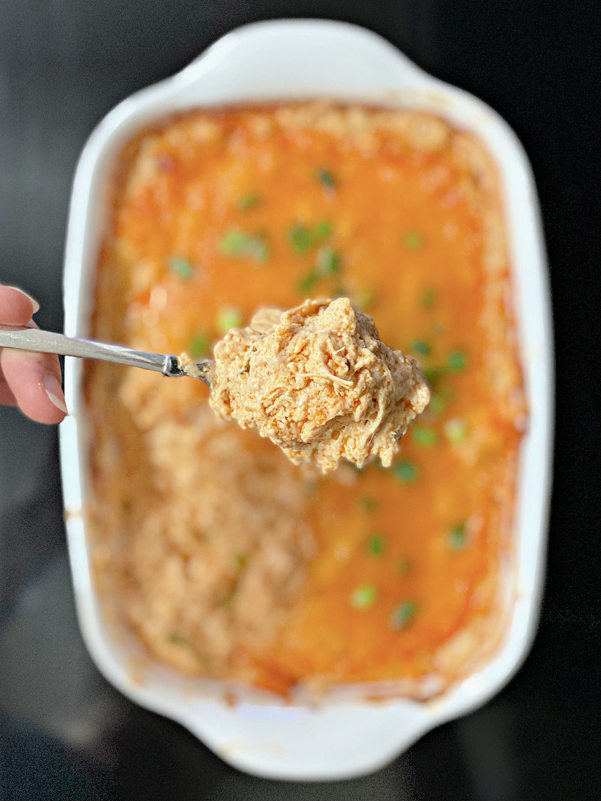 Woman holding a spoon full of chicken dip.