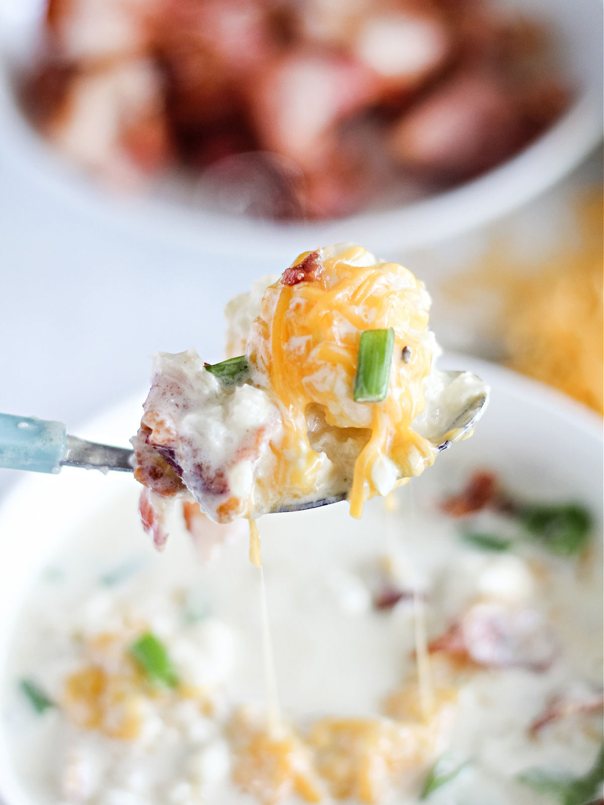 A spoon with cheesy cauliflower soup with green onions and bacon.