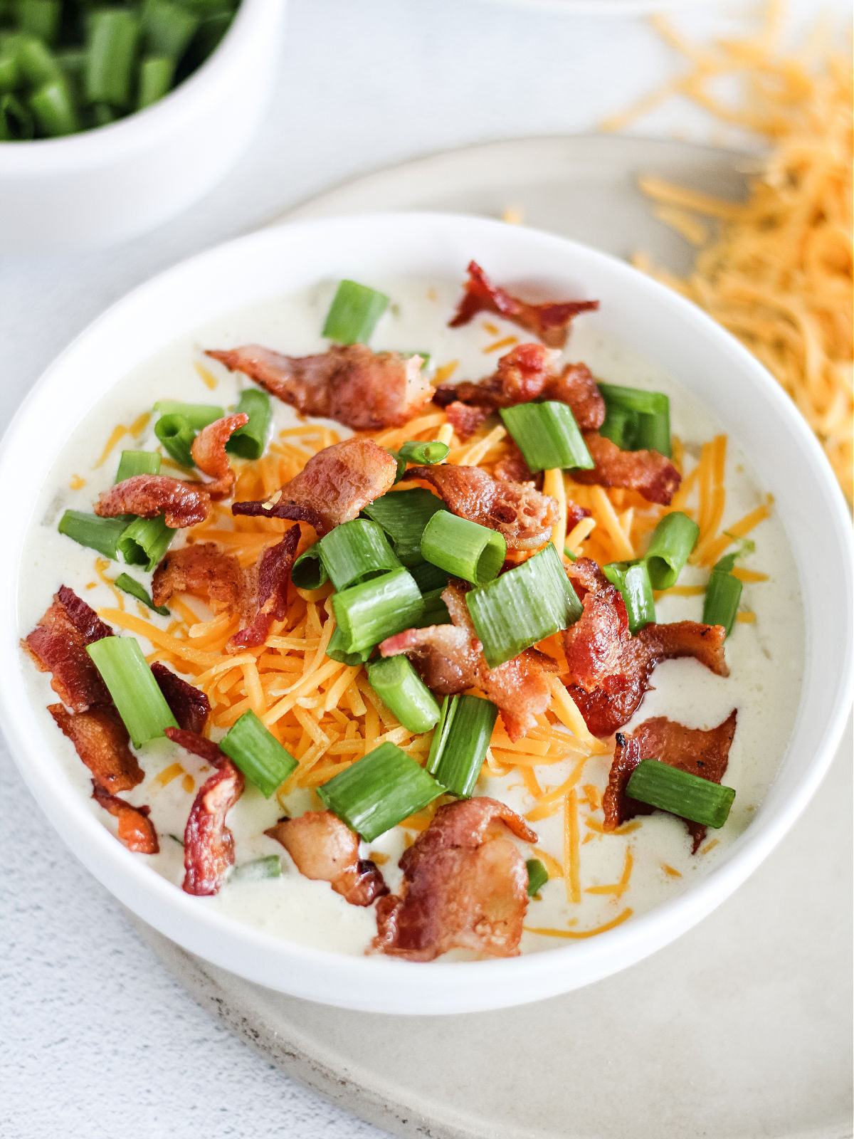 White bowl filled with cauliflower soup topped with bacon, Cheddar cheese, and green onions.