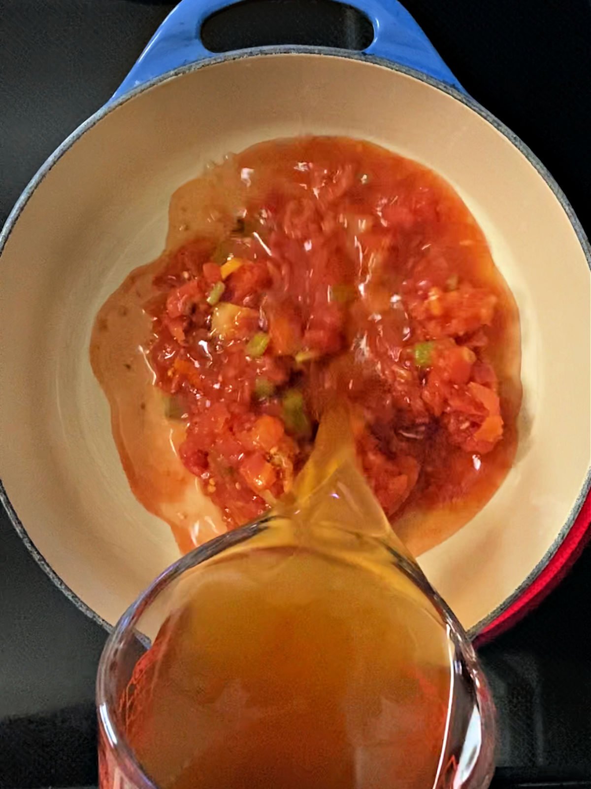 Pouring broth over tomatoes in a Dutch oven.