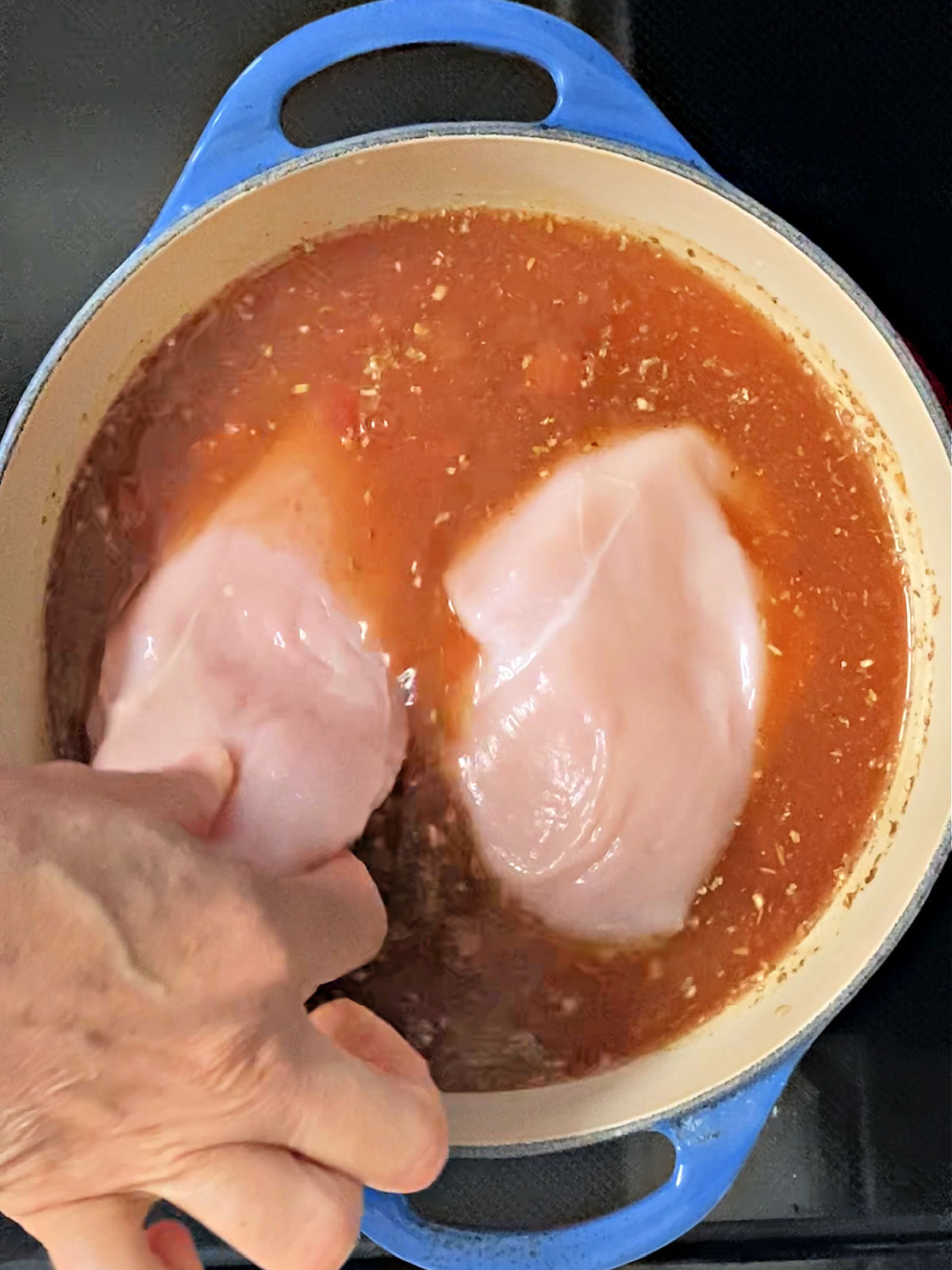 Woman's hand placing chicken breasts into a pot of soup.