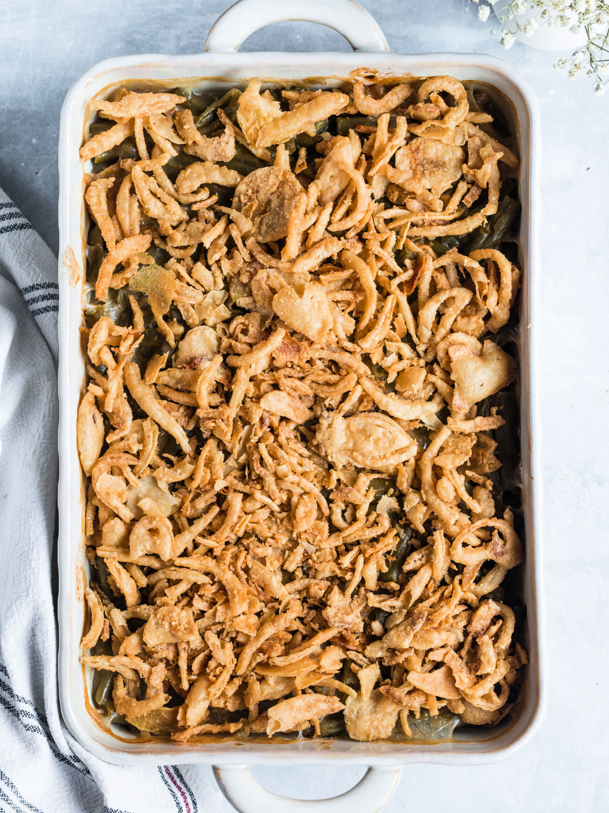 French fried onions on top of green beans in a white baking dish.