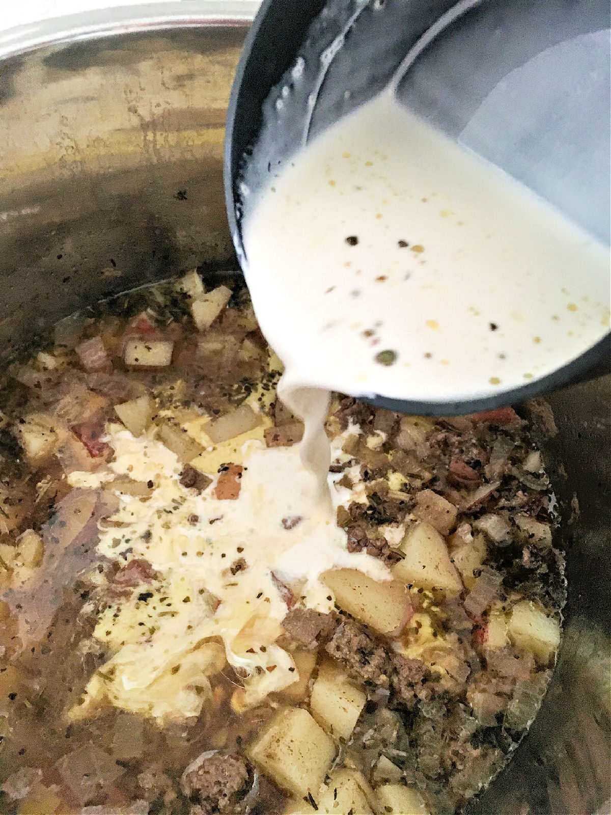 Pouring cream into an Instant Pot filled with beef, potatoes, and onions.