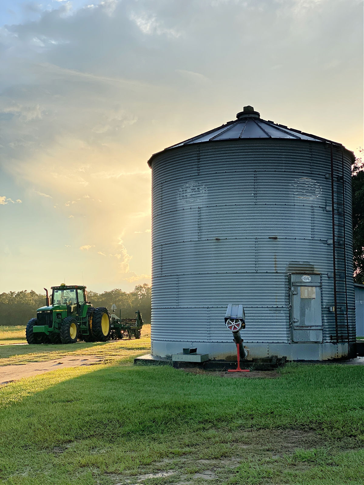 Sun setting behind a silo by a John Deere tractor.