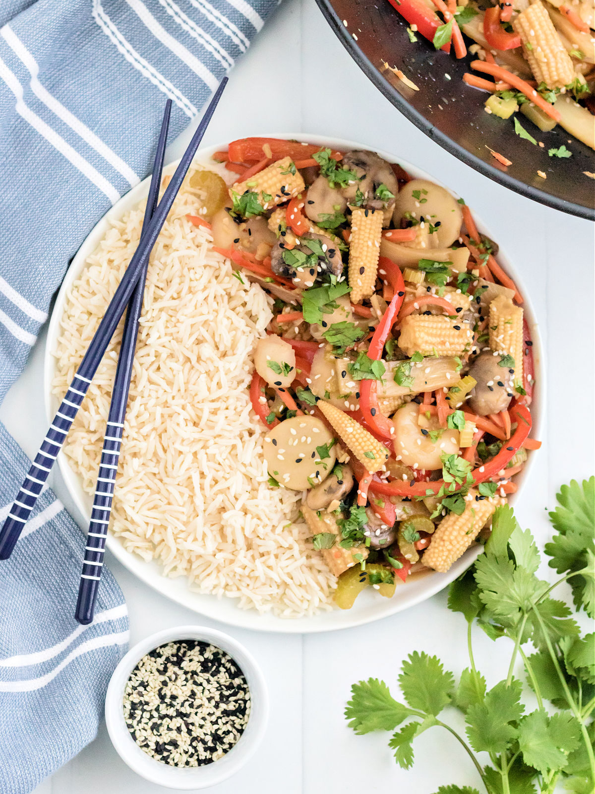 Stir fry veggies in a bowl with white rice and chop sticks..