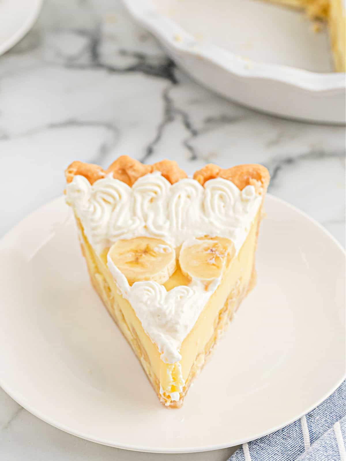 Slice of banana cream pie topped with whipped cream and bananas.