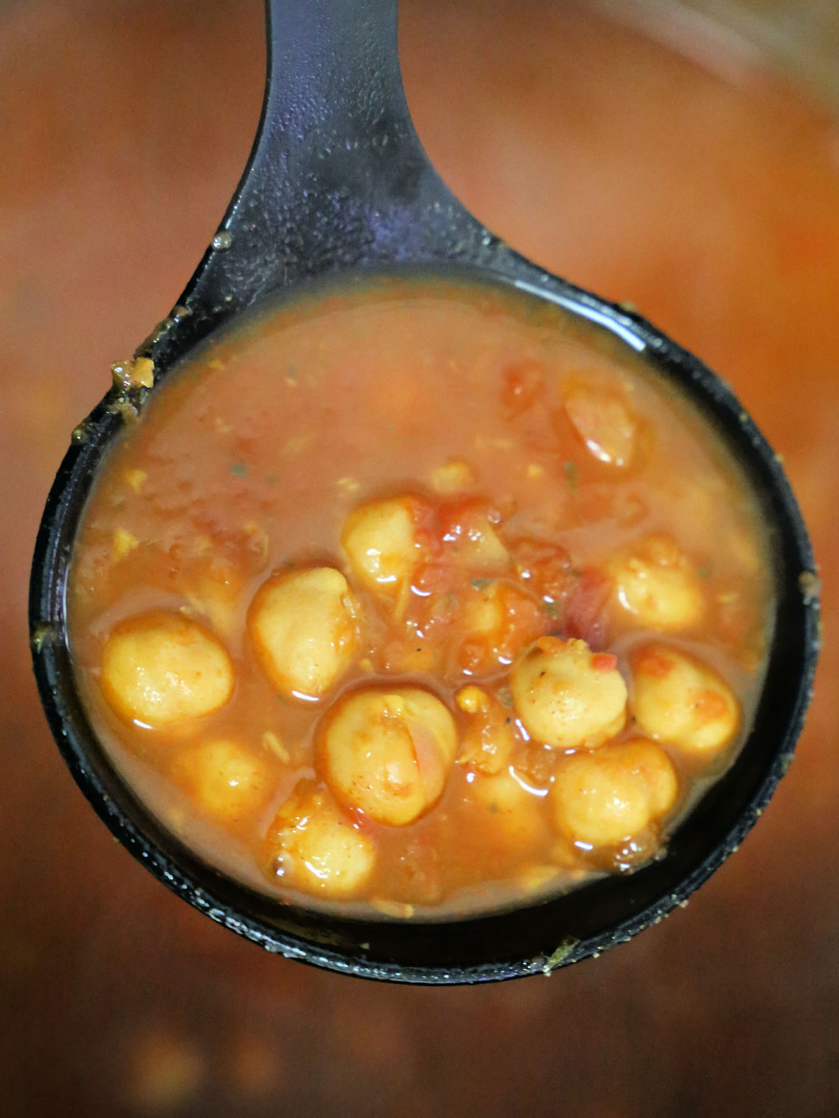 Scoop of chana masala in a black ladle.