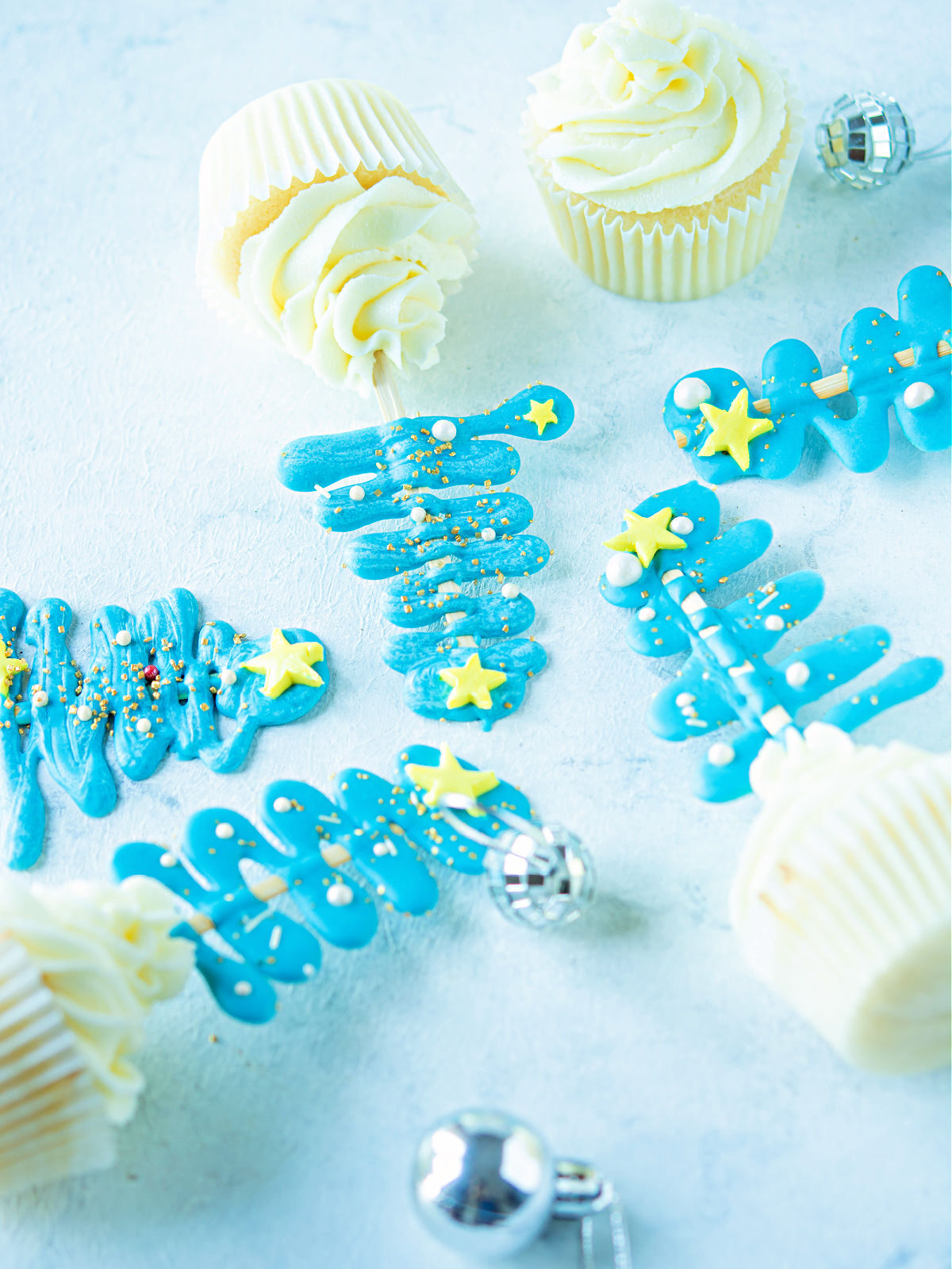 Vanilla cupcakes with blue Christmas tree toppers.