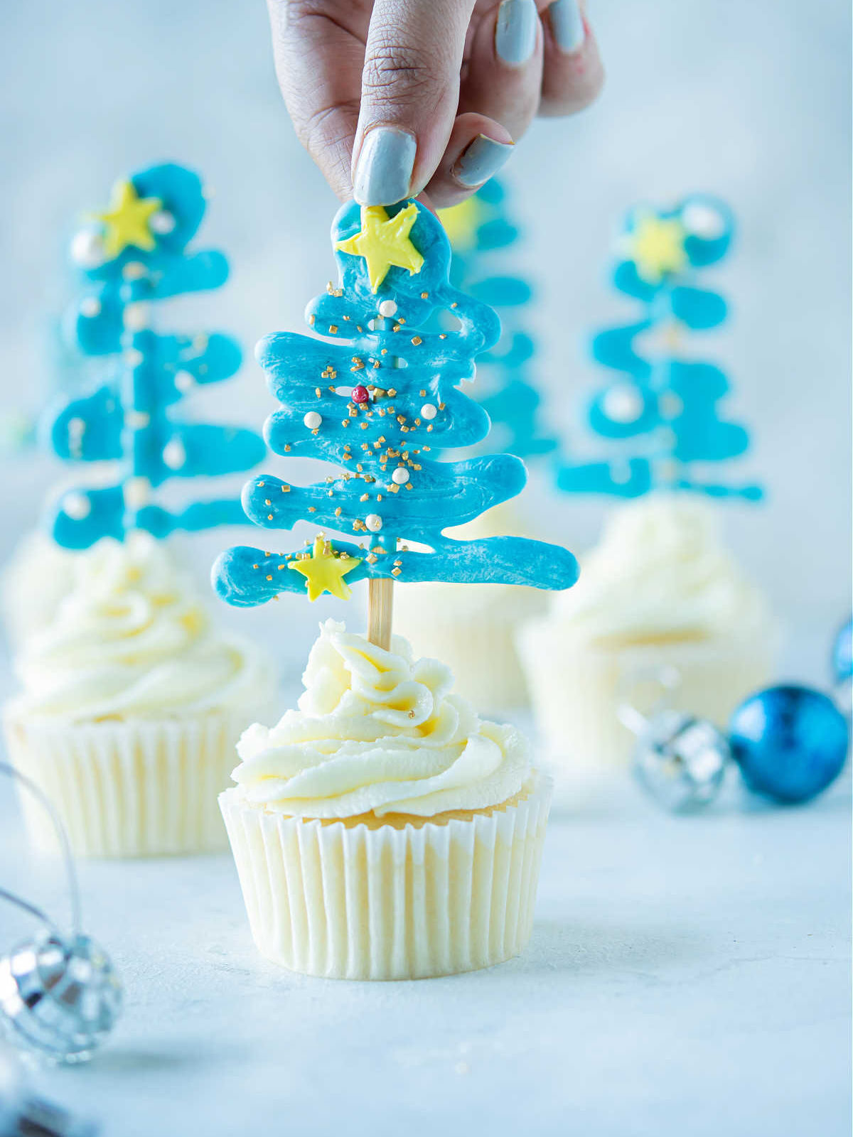 Woman placing cupcake topper into vanilla cupcake.