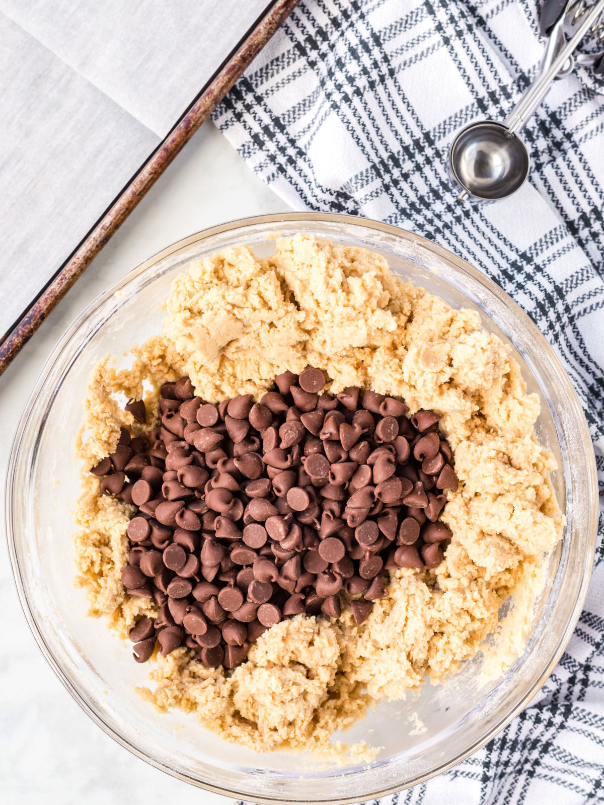 Chocolate chips on top of cookie dough in a glass mixing bowl.
