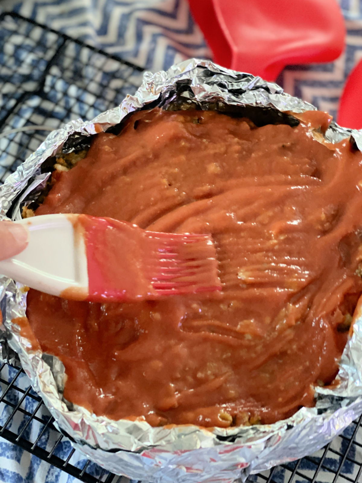 Brushing the top of a meatloaf with a ketchup mixture.