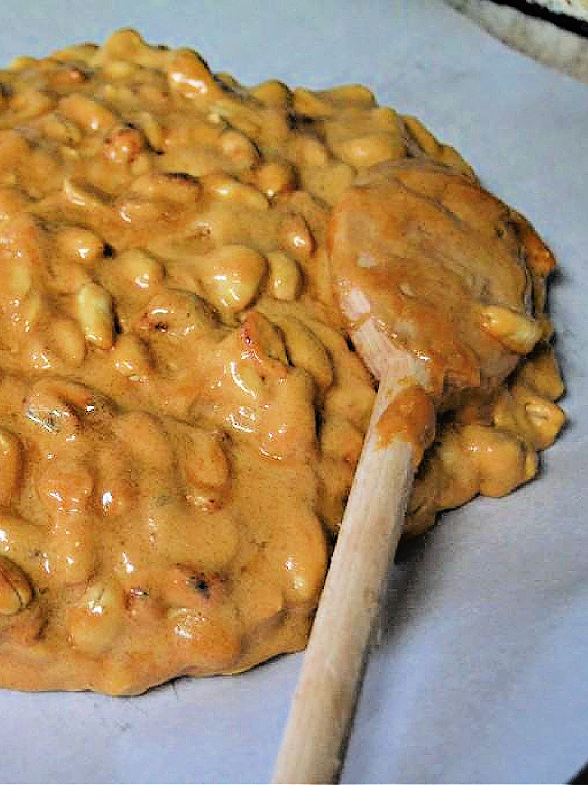 Spreading peanut brittle on a parchment lined cookie sheet.
